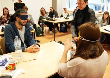 2 Schüler haben die Augen verbunden und schenken ein Glas Wasser ein.